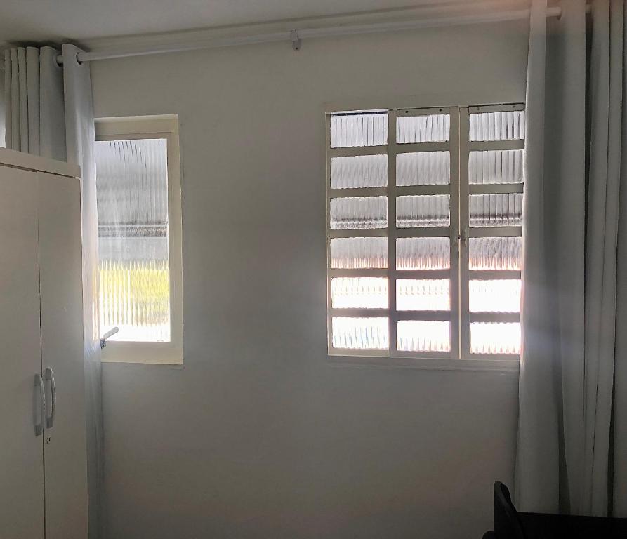 Pousada 714 في برازيليا: غرفة بيضاء مع نافذتين وباب