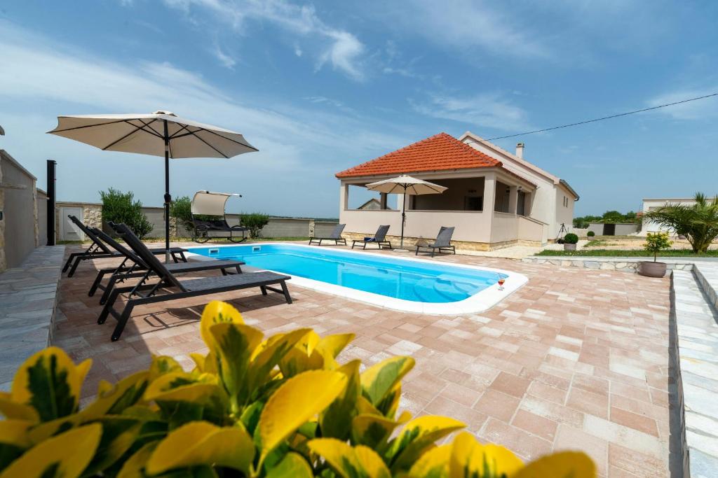 a swimming pool with two chairs and an umbrella at Villa Zrilic ZadarVillas in Perušić Benkovački