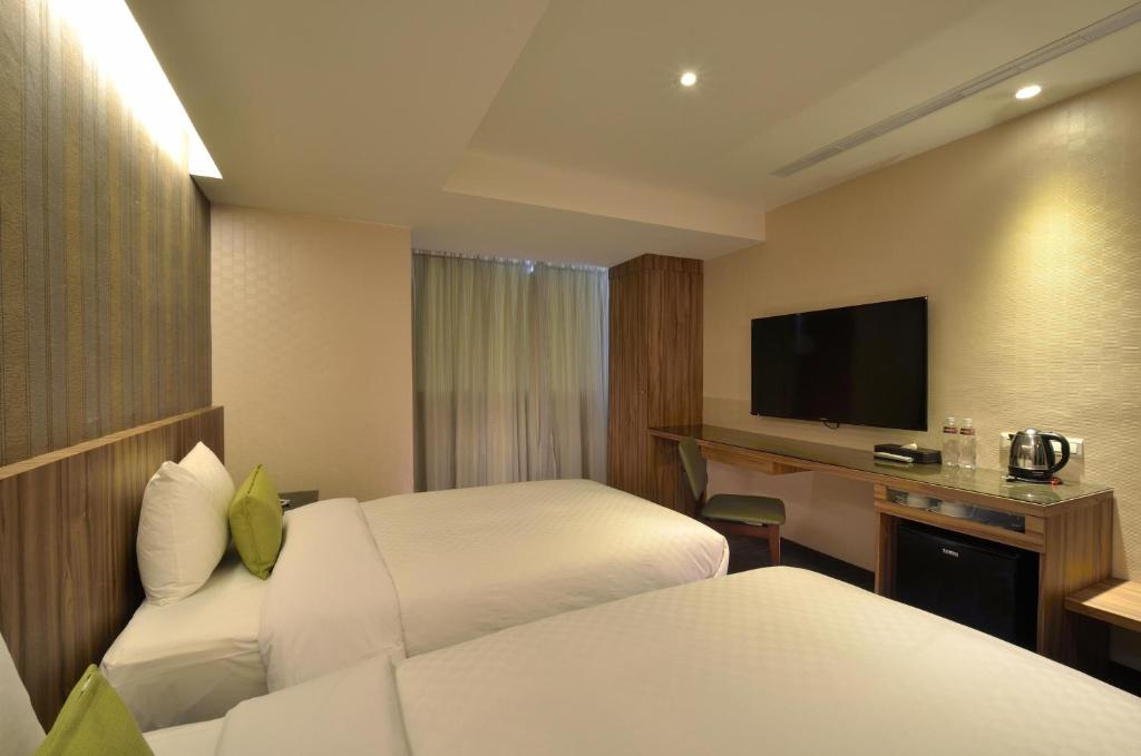 Una habitación de hotel con dos camas y un escritorio con televisión. en 欣欣時尚旅店松山站, en Taipéi