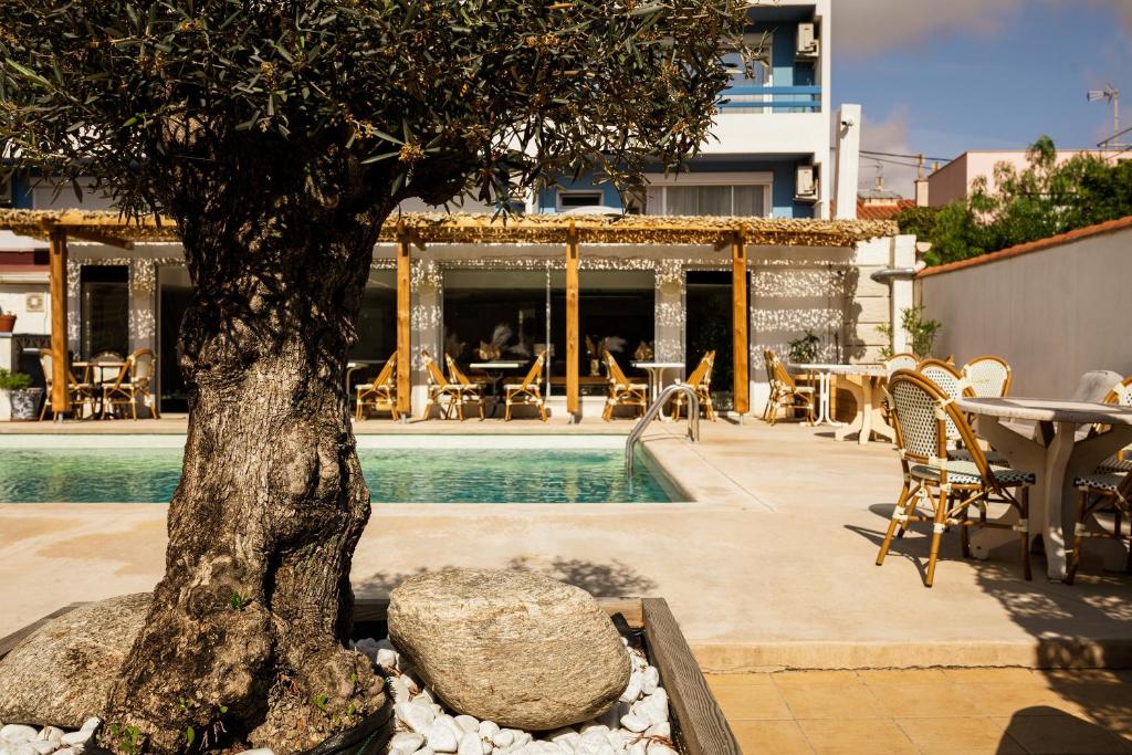 een boom naast een zwembad met een tafel en stoelen bij Hôtel Les Sables - Urban Style - by Logis Hotels in Canet-en-Roussillon