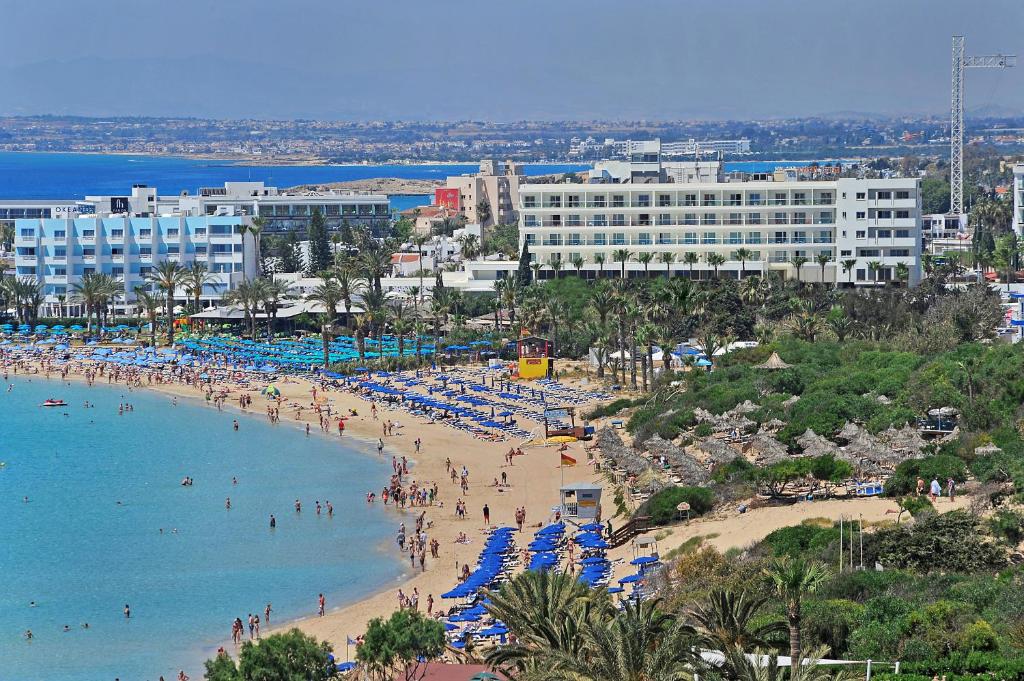 a beach with blue chairs and people in the water at Nelia Beach Hotel & Spa in Ayia Napa