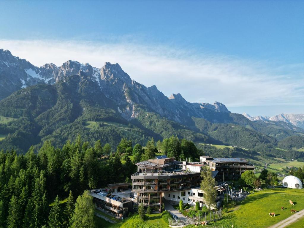 a building on a hill with mountains in the background at Holzhotel Forsthofalm in Leogang