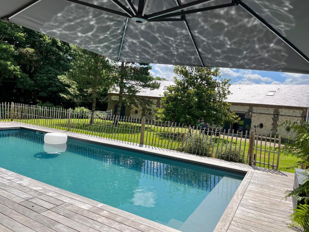 um guarda-chuva sobre uma piscina num quintal em Le Grenier d'Ouilly au cœur du Pays d'Auge - Gîte avec piscine à 20 min des plages em Ouilly-le-Vicomte