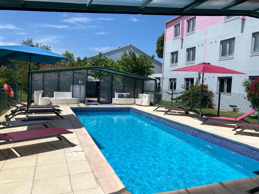 a swimming pool with chairs and umbrellas next to a building at Kyriad Montpellier Aéroport - Parc Expo in Mauguio