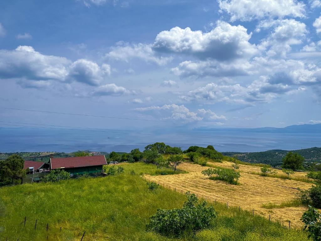 a field with a house and a barn in the distance at Assos Sizin Ev in Ayvacık