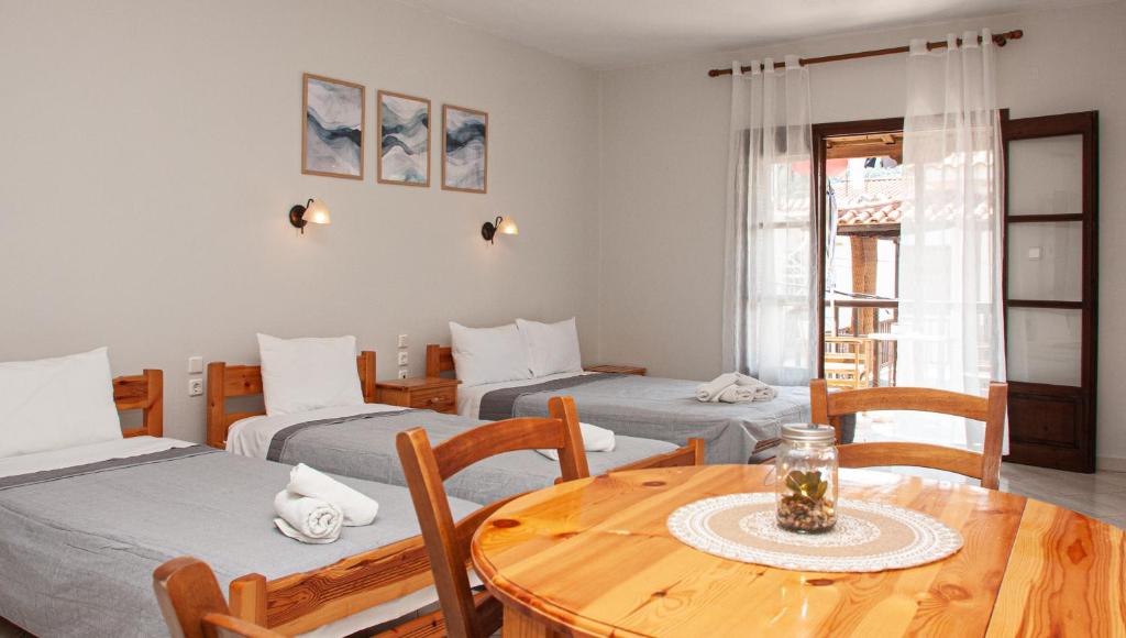 Habitación con 3 camas, mesa, mesa y sillas. en Aris Junior Studios Neo Klima Skopelos, en Neo Klima