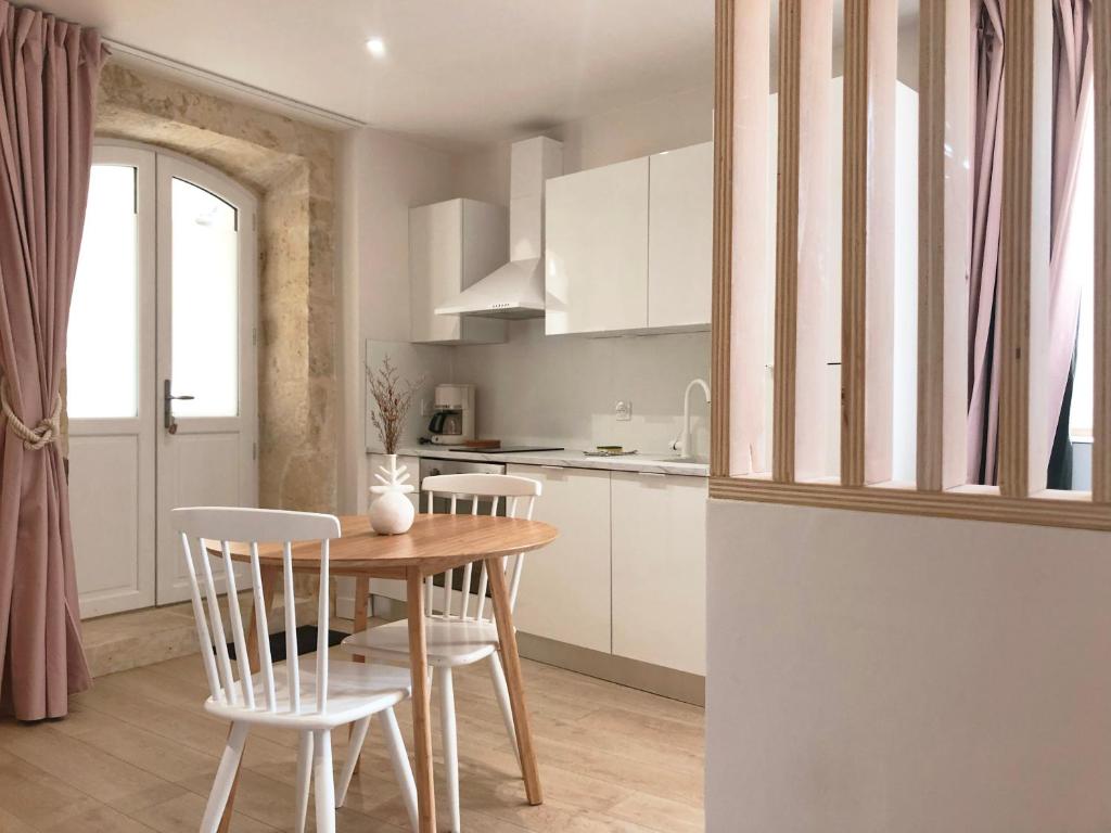una cocina con armarios blancos y una mesa y sillas de madera. en Le Seize - Studio dans le centre historique d'Auch, en Auch