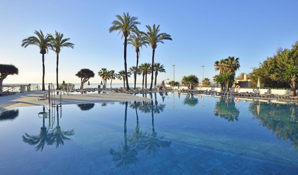 a large swimming pool with palm trees and a beach at Hotel Ocean House Costa del Sol, Affiliated by Meliá in Torremolinos