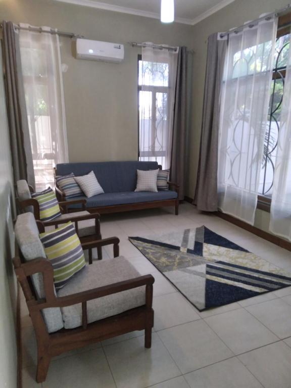 a living room with a couch and chairs and windows at Modern 2 BR home w/ 3 ACs, 2 TVs near the beach in Dar es Salaam