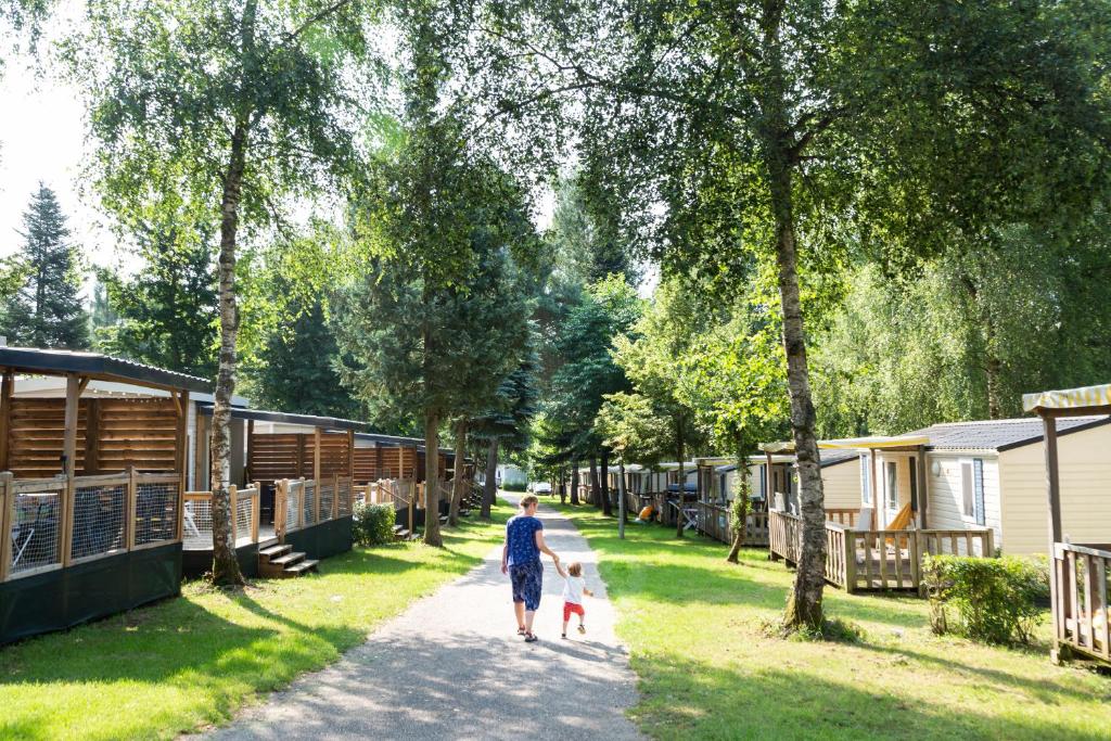 a person walking two dogs down a path near some campsites at hu Birkelt Village in Luxembourg