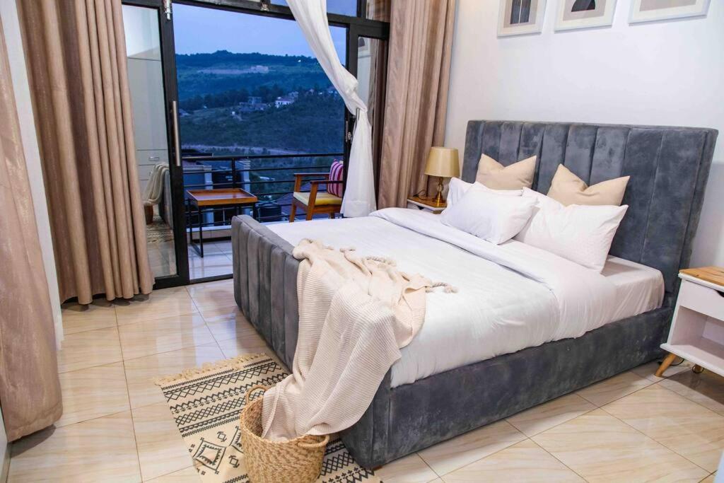 een slaapkamer met een groot bed en een groot raam bij Nzuri Nest Apartments Zuba in Kigali