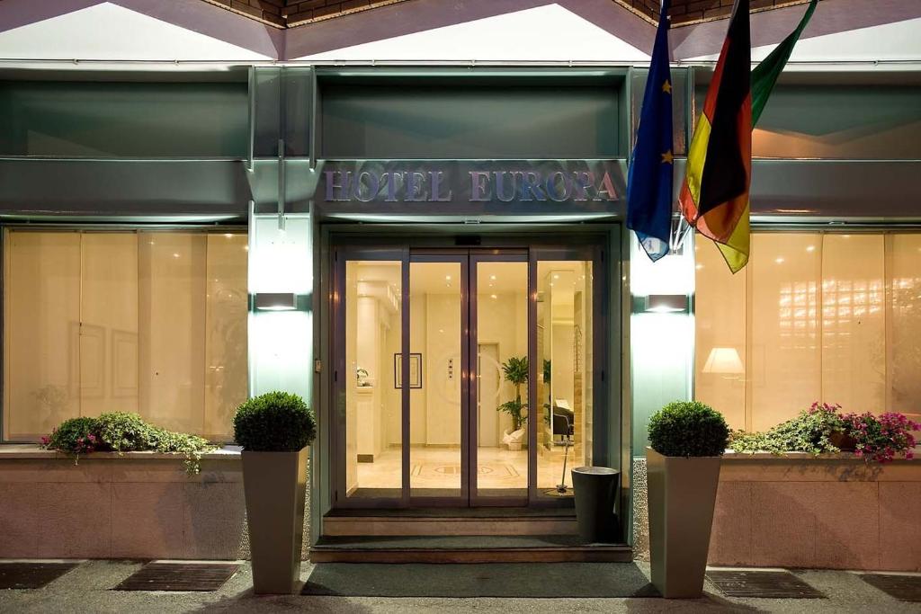 una puerta delantera de un edificio con banderas y plantas en Hotel Europa, en Alessandria