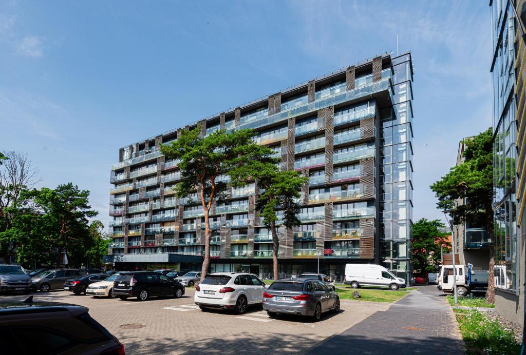 a tall building with cars parked in a parking lot at PALANGA DAUKANTO APARTAMENTAI in Palanga