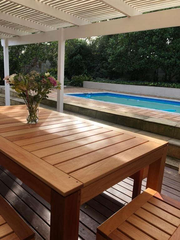 uma mesa de madeira num deque ao lado de uma piscina em Stylish house/Heated swimming pool-5min to Beach em Wilderness