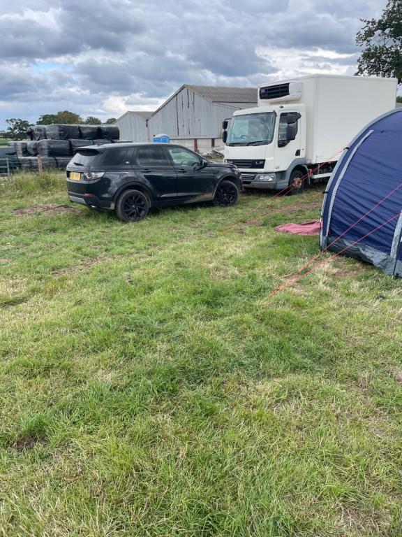 a black car parked next to a trailer and a truck at Dadford campsite in Silverstone