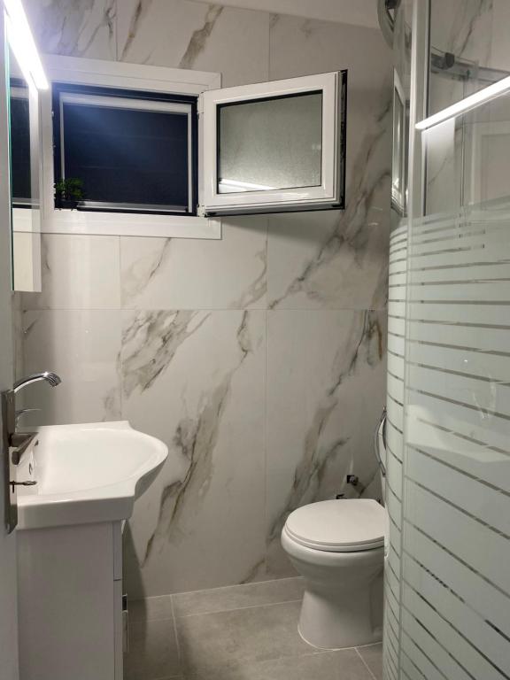 a white bathroom with a toilet and a sink at Aggelikas apartments in Paleokastritsa