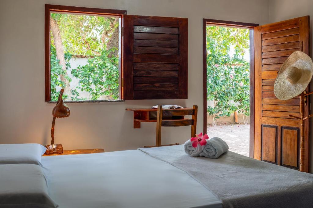 a bedroom with a bed and a table and windows at Pousada Flambaião in Jijoca de Jericoacoara