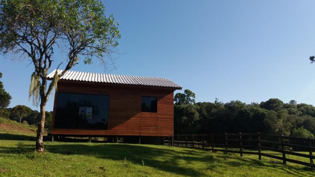 a wooden cabin in a field with a tree at Cabana Entre Lagos in São Joaquim
