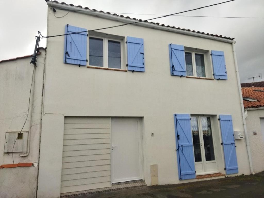 ein weißes Haus mit blauen Rollläden und einer Garage in der Unterkunft Maison La Tranche-sur-Mer, 3 pièces, 5 personnes - FR-1-194-267 in La Tranche-sur-Mer