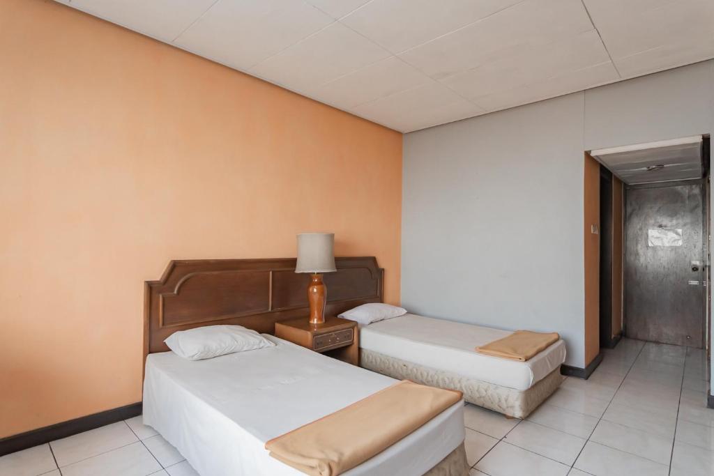 a hotel room with two beds and a lamp at Istana Hotel Bandung Mitra RedDoorz in Bandung