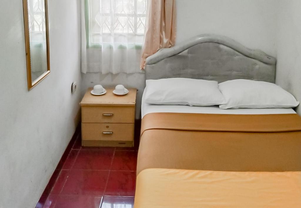 a small bedroom with two beds and a night stand at Villa Anyelir Yustik Mitra RedDoorz in Selabintana