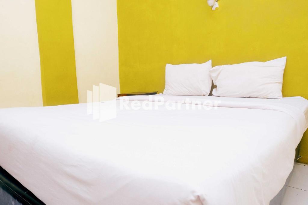 Hotel Permata Makassar Mitra RedDoorz في Balangberu: سرير بشرشف ووسائد بيضاء في الغرفة