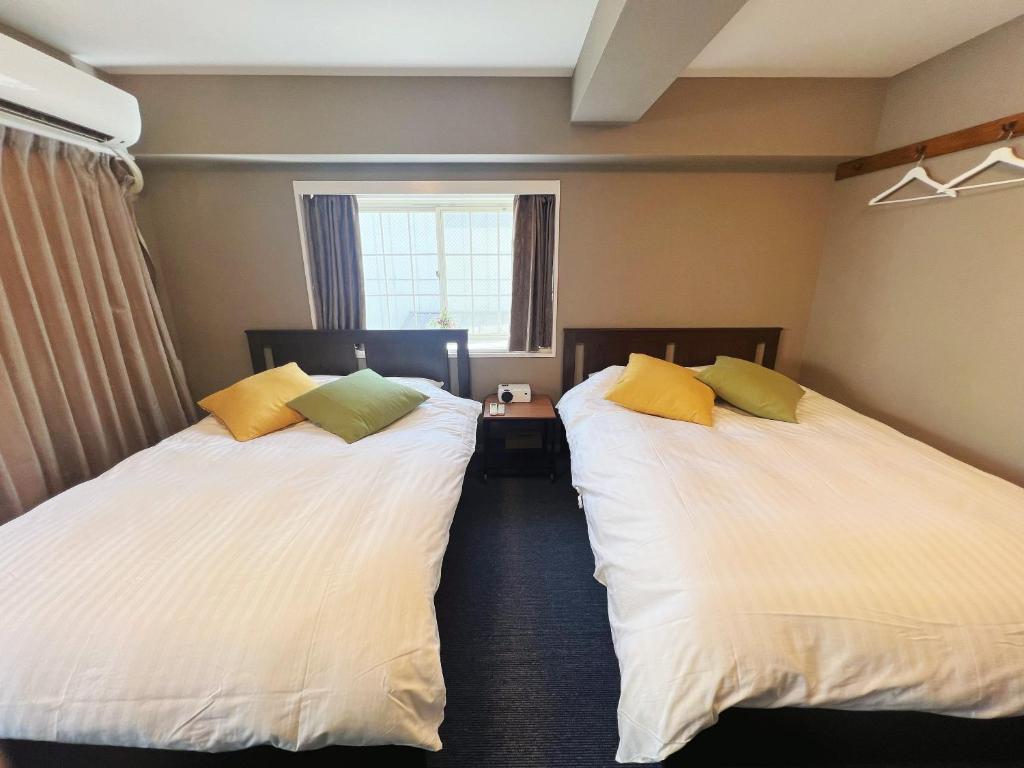 Cette chambre comprend 2 lits avec des draps blancs et des oreillers jaunes. dans l'établissement 四季の彩　浅草宿, à Tokyo