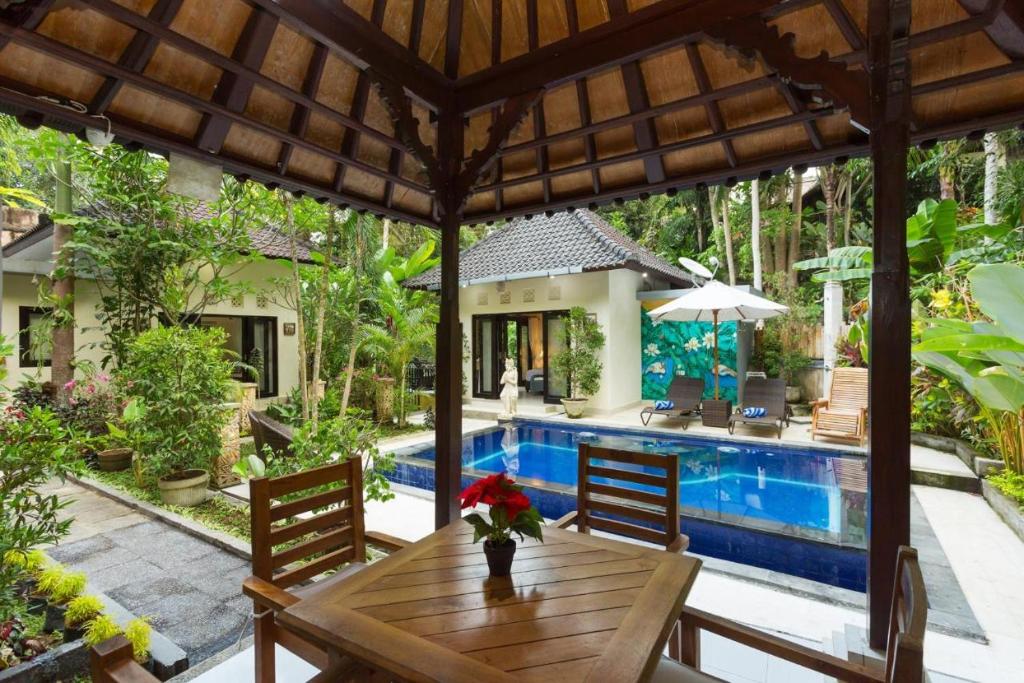 patio z drewnianym stołem i basenem w obiekcie Bakti Villa w mieście Ubud