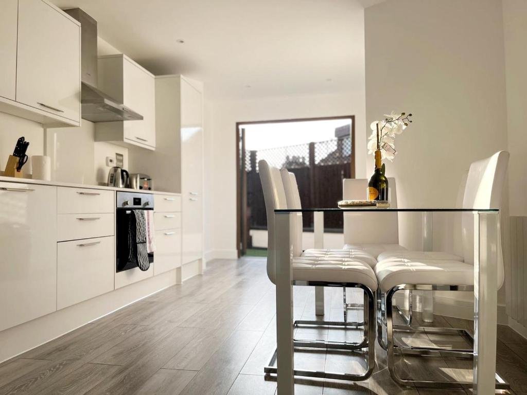 cocina con mesa de cristal y armarios blancos en Spacious 3 bed 3 bath Duplex Apartment - 18 mins from Central London - Sleeps 8, en Watford