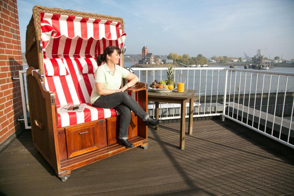 een vrouw in een grote schommelstoel op een balkon bij Hotel AM ELBUFER in Hamburg