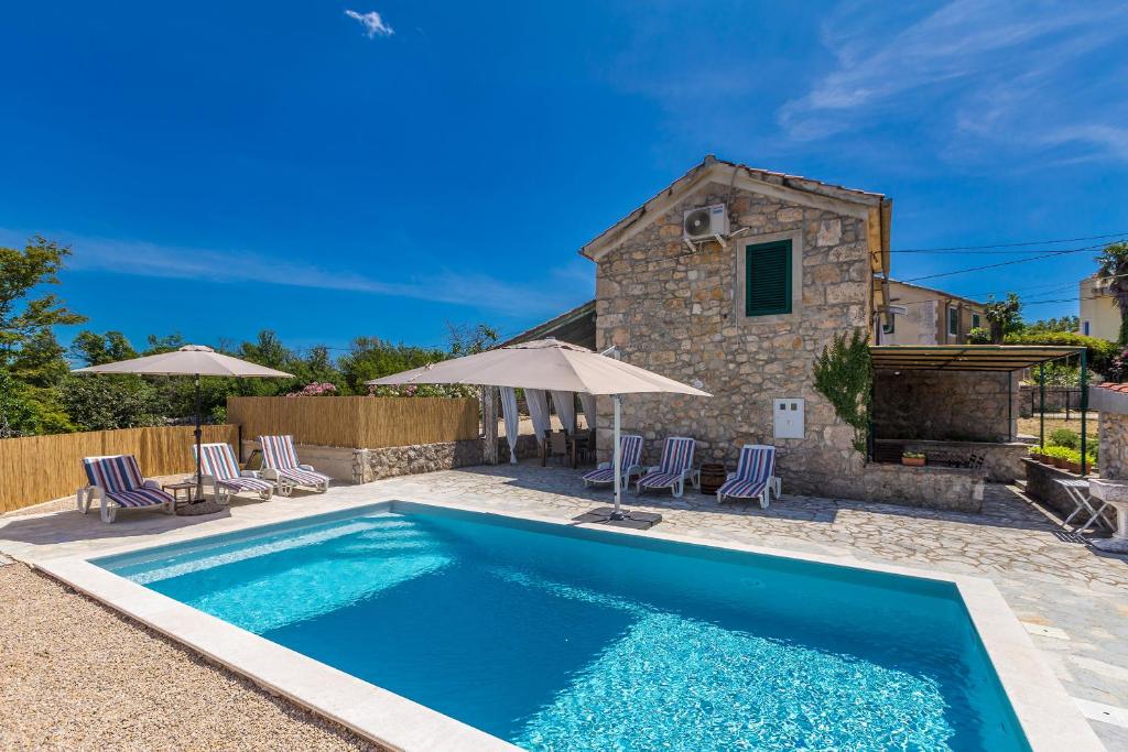 a pool in front of a house with chairs and umbrellas at Holiday house EDEN in Rasopasno