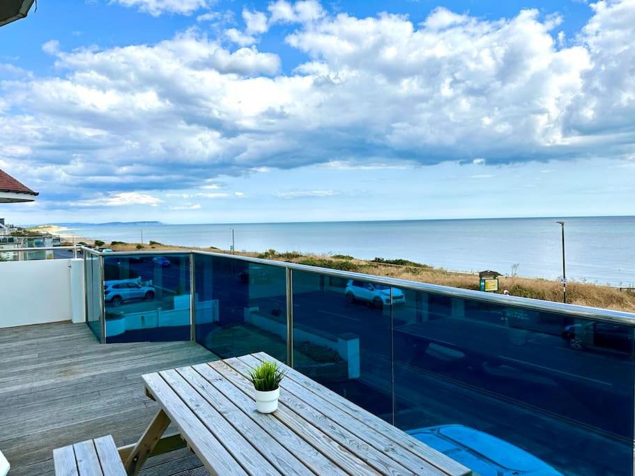 a balcony with a wooden table and a view of the ocean at Stunning Panoramic Sea View Beach Location - Sleeps up to 4 People - Free Parking - The Best Beach! - Great Location - Fast WiFi - Smart TV - Newly decorated - sleeps up to 4! Close to Bournemouth & Poole Town Centre & Sandbanks in Bournemouth