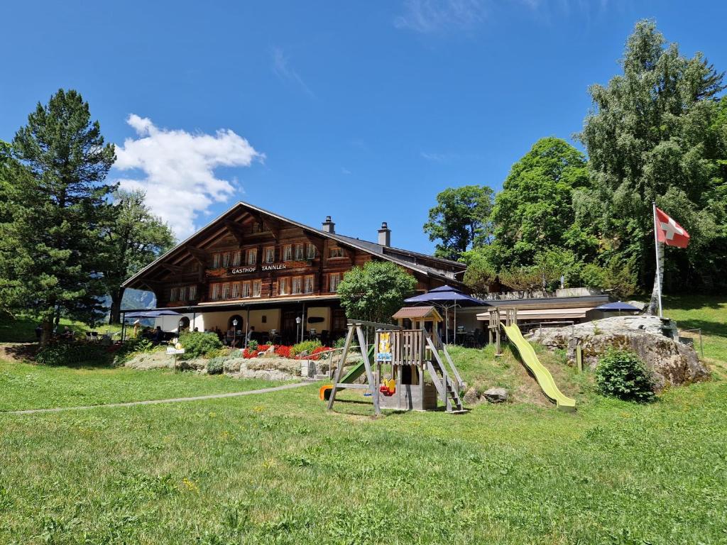 une grande maison en bois avec une aire de jeux en face de celle-ci dans l'établissement Landgasthof Tännler, à Innertkirchen