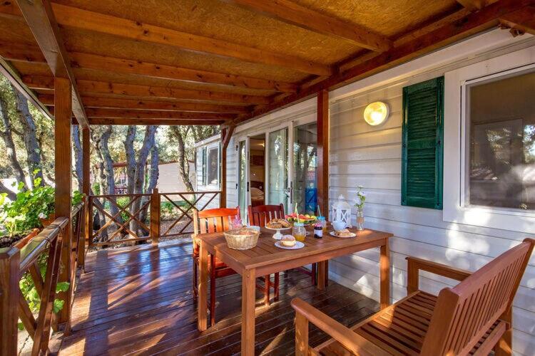 une terrasse couverte d'une maison avec une table et des chaises en bois dans l'établissement Mobile homes Rosemary in camping Strasko Novalja, à Novalja