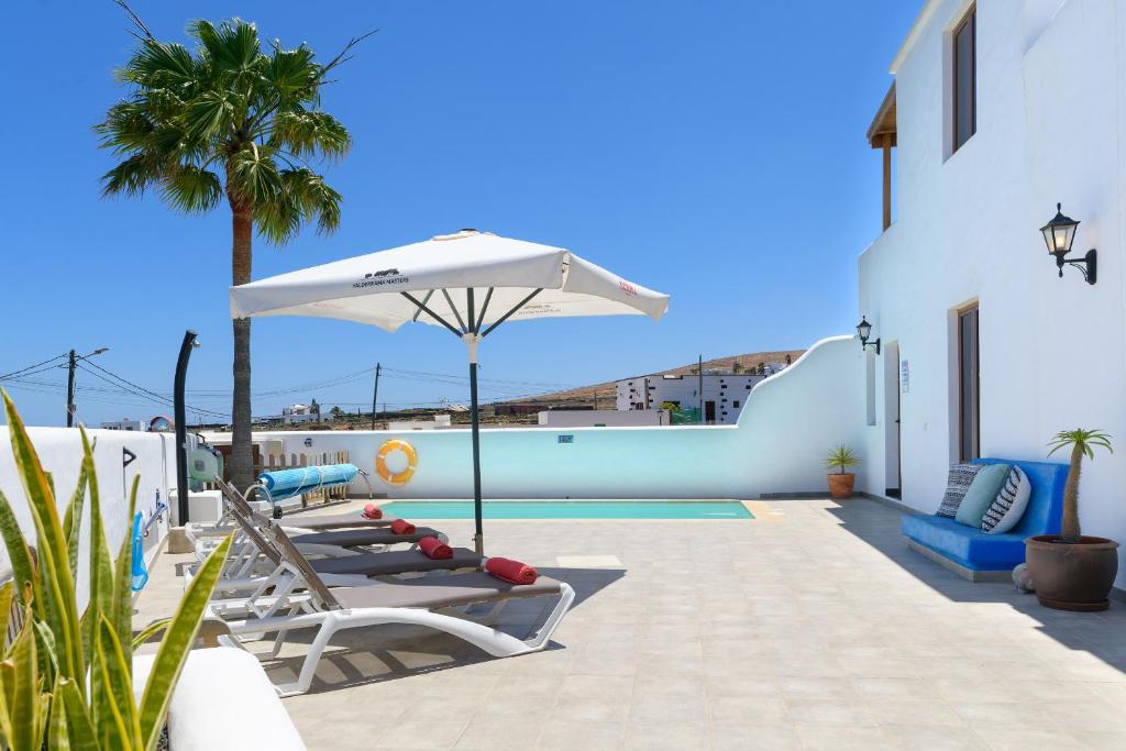 a patio with lounge chairs and an umbrella and a pool at Casa El Patio Teseguite in Teseguite