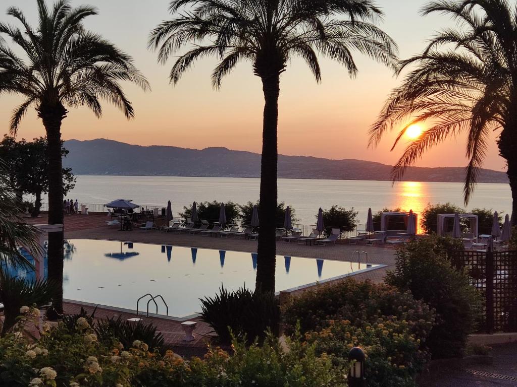 a view of the water and palm trees at sunset at Altafiumara Resort & Spa in Villa San Giovanni