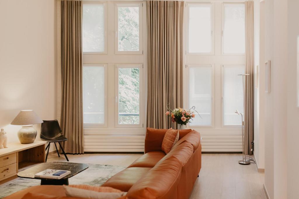 a living room with a brown couch and windows at Blue Bird Residence Wijngaard in Antwerp