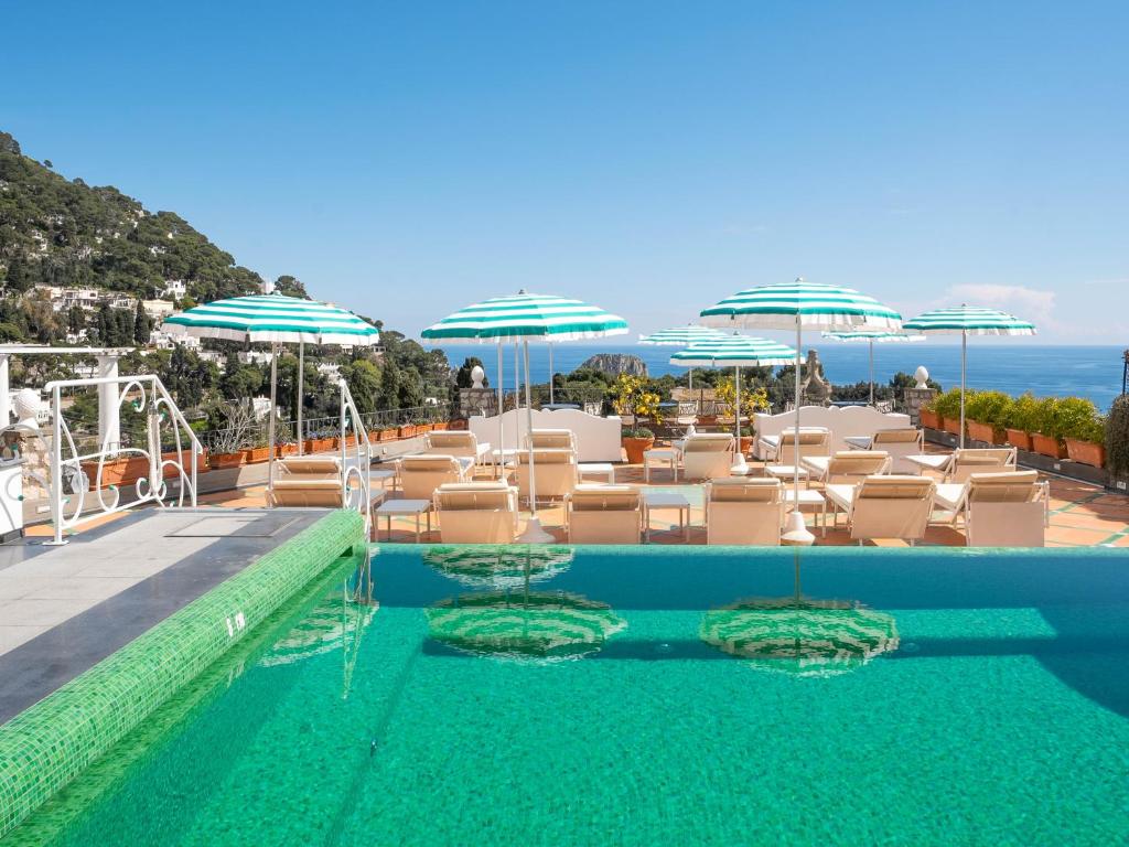 a swimming pool with chairs and umbrellas and the ocean at Sina Flora in Capri