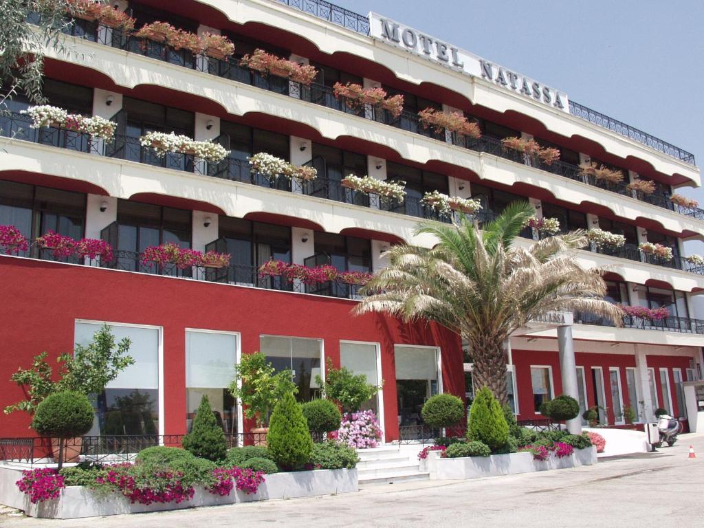 a red building with potted plants and a palm tree at Natassa Hotel in Xanthi