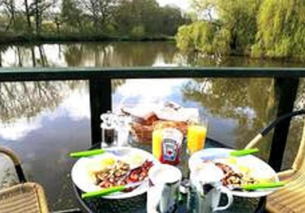 einen Tisch mit Speisen und Getränken neben einem Fluss in der Unterkunft Snug & Secluded Lakeside Shepherds Hut 'Carp' in Uckfield