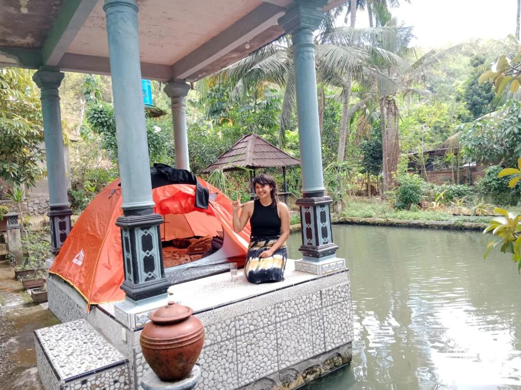 a woman sitting on a porch next to a river at Gecko Tropical inn in Gerung