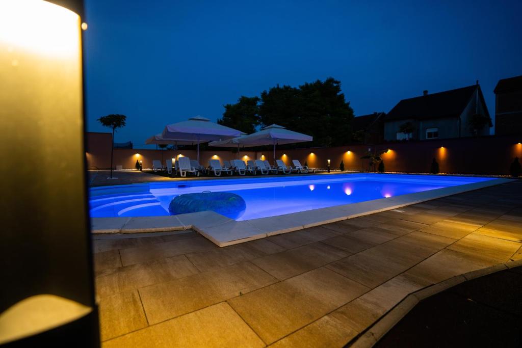 a swimming pool at night with chairs and umbrellas at Villa Biser Dunava in Vukovar