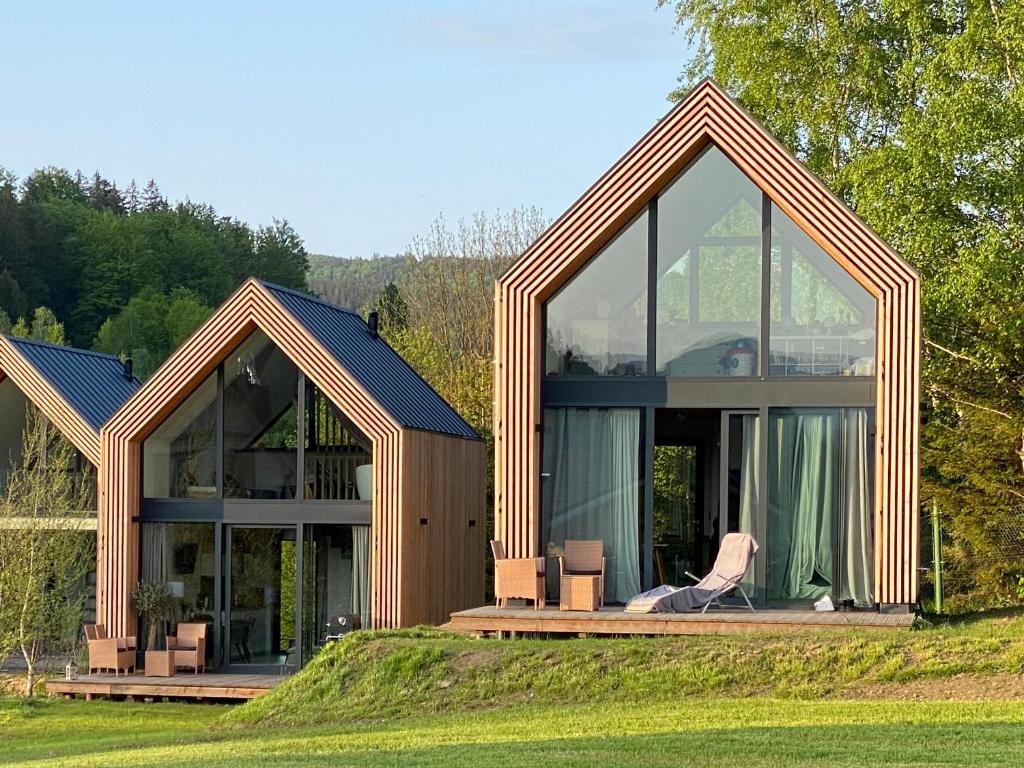 una casa con finestre in vetro e una sedia su un campo di Domki Pod Lasem - Domek Sosnowy a Stronie Śląskie