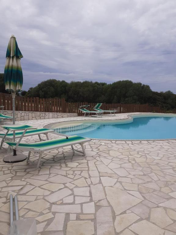 a swimming pool with two chairs and an umbrella at Agriturismo Gli Olivastri con piscina,solarium, vista mare ,sole -mare e tanta natura ,climatizzatore,wifi in Aglientu