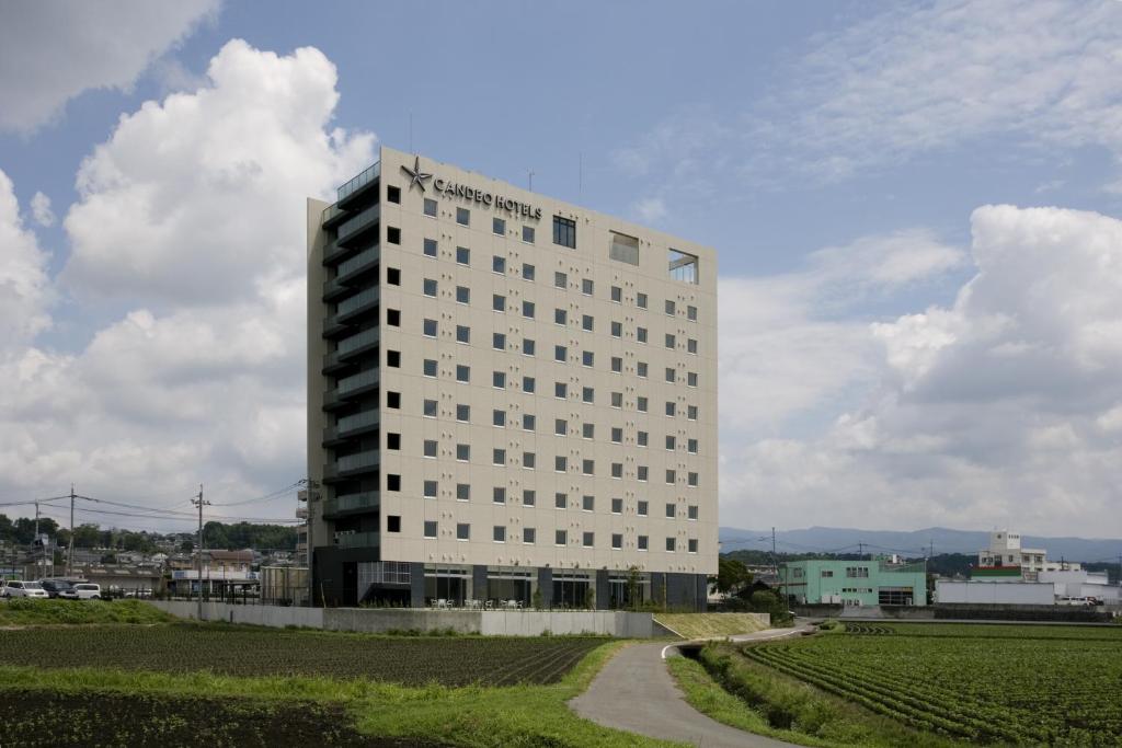 a tall white building in the middle of a field at Candeo Hotels Ozu Kumamoto Airport in Ozu