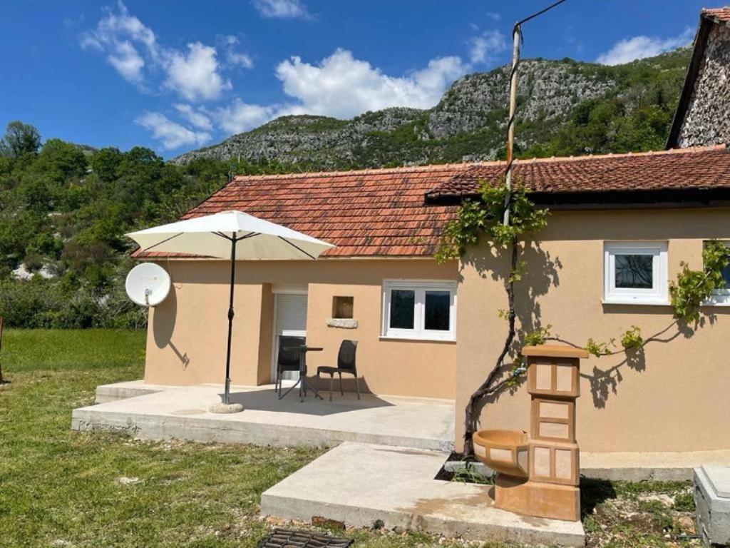 ein Haus mit einem Regenschirm, einem Tisch und Stühlen in der Unterkunft Holiday house ISIDORA in Danilovgrad