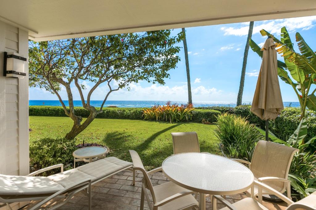 d'une terrasse avec tables et chaises et vue sur l'océan. dans l'établissement Oceanfront Corner Villa w Air Conditioning - Alekona Kauai, à Koloa