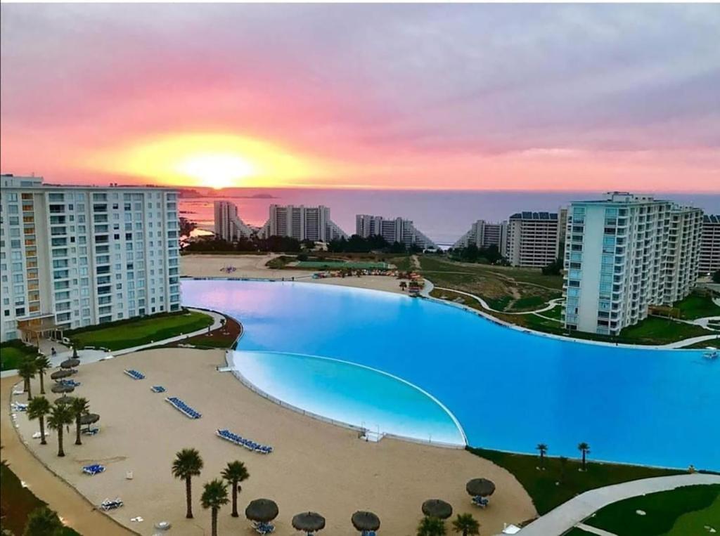 a large swimming pool with a sunset in the background at Departamento Laguna Bahía Algarrobo in Algarrobo