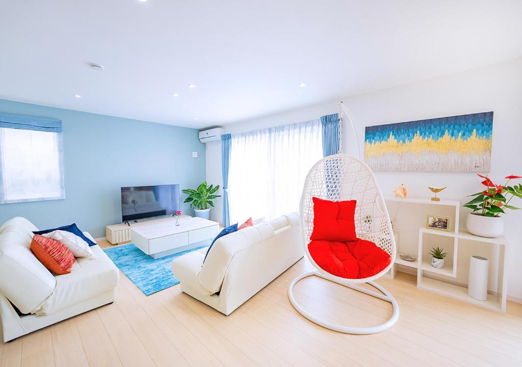 Elle comprend un salon doté d'un mobilier blanc et d'une chaise rouge. dans l'établissement ヴィラアマルフィ パームスプリングス宮古島リゾート, à Île Miyako