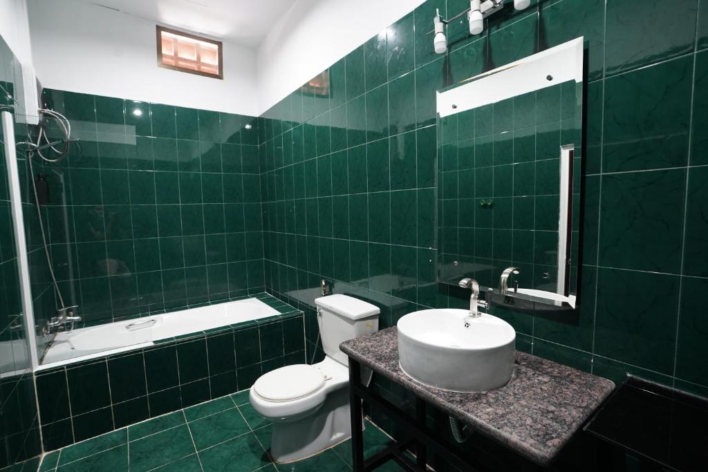 a green tiled bathroom with a toilet and a sink at Birdcage Boutique in Phnom Penh